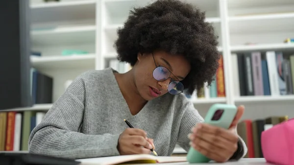 African American Woman Student Using Smartphone Writing Notebook Library University — Stockfoto