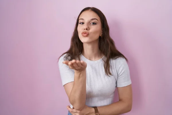 stock image Young hispanic girl standing over pink background looking at the camera blowing a kiss with hand on air being lovely and sexy. love expression. 