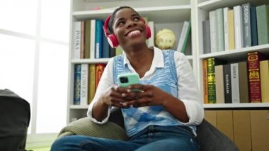 Afrikalı Amerikalı bir kız öğrenci kütüphanede müzik dinlerken kendinden emin bir şekilde gülümsüyor.