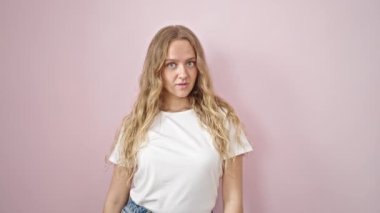 Young blonde woman standing with surprise expression over isolated pink background
