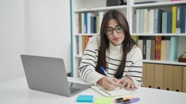 Genç, güzel İspanyol bir öğrenci kütüphanede dizüstü bilgisayar kullanıyor.