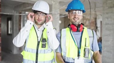 İnşaat alanında kollarını kavuşturup gülümseyen iki adam.