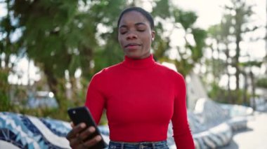 Afro-Amerikalı kadın, parkta akıllı telefonun yanında kendinden emin bir şekilde selfie çekiyor.