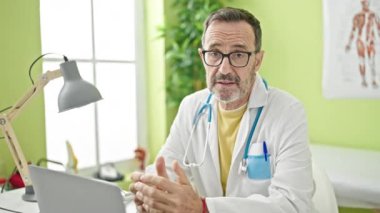 Orta yaşlı doktor klinikte dizüstü bilgisayarla konuşuyor.