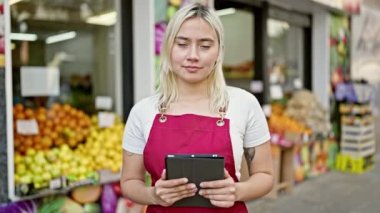Genç ve güzel İspanyol kadın önlük giyiyor. Meyve dükkanında dokunmatik ped kullanıyor.