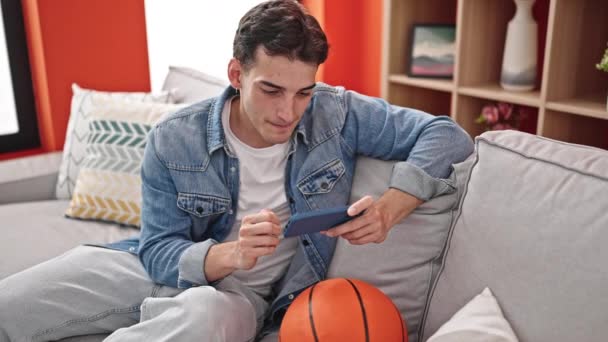 Jonge Spaanse Man Kijken Basketbal Wedstrijd Smartphone Thuis — Stockvideo