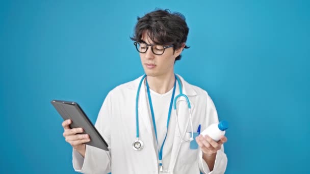 年轻的他的惊慌失措的医生用触摸板把药瓶放在孤立的蓝色背景上 — 图库视频影像