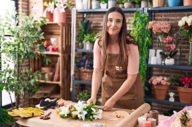 Young beautiful hispanic woman florist make bouquet of flowers at flower shop