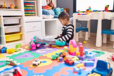 Sevimli İspanyol çocuk, anaokulunda yerde oturmuş rahat bir ifadeyle oynuyor.