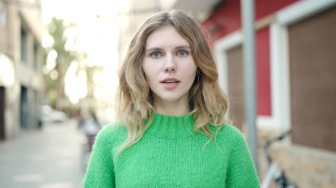 Sokakta ciddi bir ifadeyle duran genç sarışın kadın.