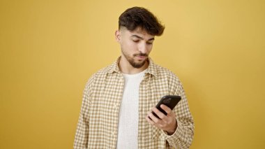Genç Arap adam, izole edilmiş sarı arka plan üzerinde akıllı telefon kullanıyor.