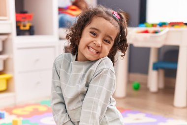 Adorable hispanic girl smiling confident sitting on floor at kindergarten