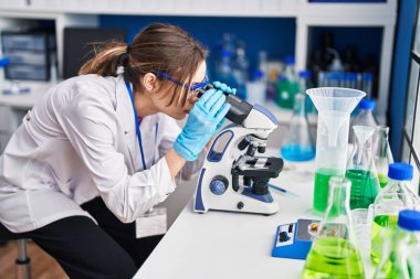 Laboratuvarda mikroskop kullanan genç ve güzel İspanyol bilim kadını.