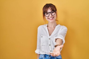 Sarı arka planda rahat gömlekler giyen genç ve güzel bir kadın gülümseyerek avuçlarını açıp yardım ve kabullenme teklif ediyor.. 