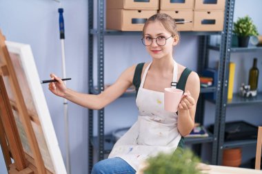 Young caucasian woman artist drinking coffee drawing at art studio