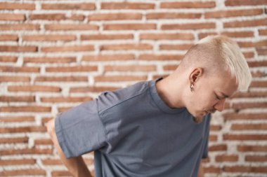 Kafkasyalı genç adam tuğlaların başında duruyor sırt ağrısı çekiyor, elleriyle dokunuyor, kas ağrısı çekiyor. 