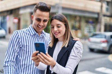 Man and woman couple hugging each other using smartphone at street