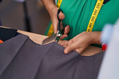 Orta yaşlı, gri saçlı kadın terzi dükkanında kumaş kesiyor.