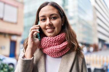 Young beautiful hispanic woman talking on smartphone wearing scarf at street