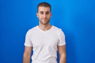 Mavi arka planda duran genç beyaz adam yüzünde ciddi bir ifadeyle rahatladı. Basit ve doğal bir şekilde kameraya bakıyorsun.. 