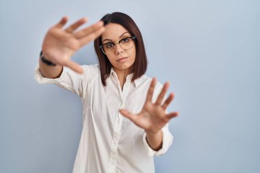 Beyaz arka planda duran genç İspanyol kadın el ve parmaklarıyla çerçeve yapıyor, kamera bakış açısı. 