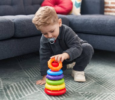 Sevimli beyaz çocuk evde yerde oturmuş basketbol oynuyor.