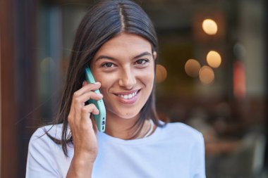 Genç, güzel, İspanyol bir kadın gülümsüyor ve caddede akıllı telefondan konuşuyor.