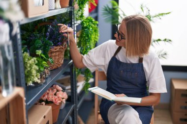 Çiçekçide kendine güvenen, gülümseyen sarışın bir kadın.