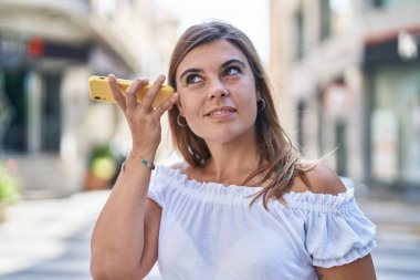Caddedeki akıllı telefondan kendine güveni tam bir sesli mesaj dinleyen genç bir kadın.