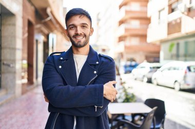 Young hispanic man standing with arms crossed gesture at coffee shop terrace