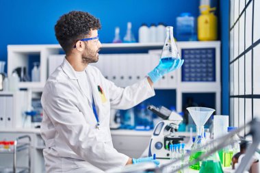 Laboratuvarda sıvı ölçen bilim adamı üniforması giyen genç bir Arap.