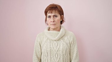Soyutlanmış pembe arka planda ciddi bir ifadeyle duran olgun İspanyol kadın.