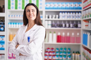 Young beautiful hispanic woman pharmacist smiling confident standing with arms crossed gesture at pharmacy