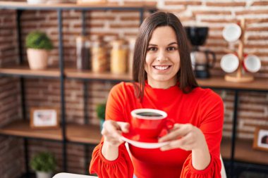 Young beautiful hispanic woman drinking coffee sitting on table at home