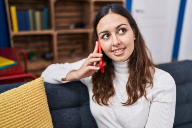Evdeki kanepede oturmuş akıllı telefondan konuşan genç, güzel İspanyol kadın.