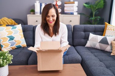 Orta yaşlı esmer kadın karton kutuyu açıyor ve kahkahalarla gülüyor.. 