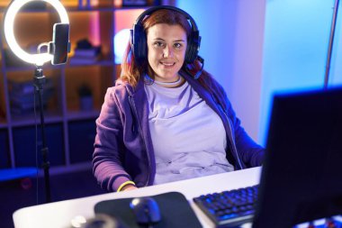 Young beautiful plus size woman streamer smiling confident sitting on table at gaming room