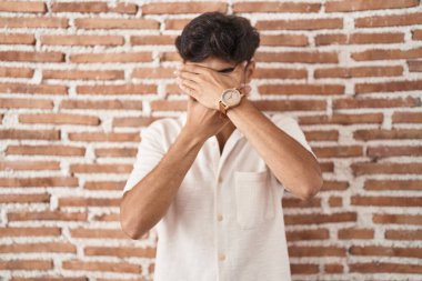 Tuğlaların arkasında duran sakallı bir Arap, gözleri ve ağzı elleriyle kapatıyor, şaşırmış ve şok olmuş. duygu gizleme 