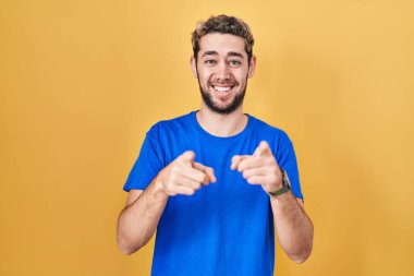 Sarı arka planda duran İspanyol sakallı adam seni ve kamerayı işaret ediyor, gülümsüyor olumlu ve neşeli. 