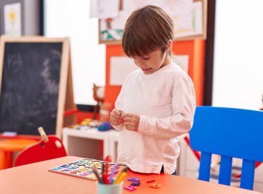 Anaokulunda masada oturmuş matematik oyunu oynayan sevimli beyaz çocuk.