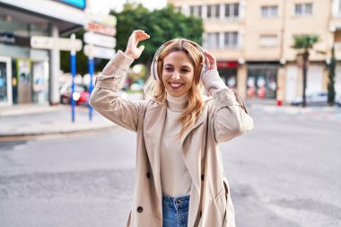 Young blonde woman listening to music and dancing at street