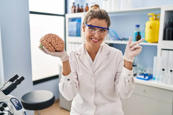 Молодая Женщина Работающая Лаборатории Держит Мозг Улыбающимся Счастливо Указывая Рукой — стоковое фото