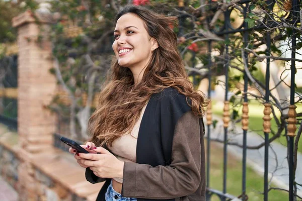 若い美しいですヒスパニック女性笑顔自信を持って使用してスマートフォンで公園 — ストック写真
