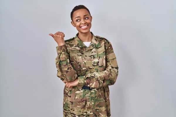 stock image Beautiful african american woman wearing camouflage army uniform smiling with happy face looking and pointing to the side with thumb up. 