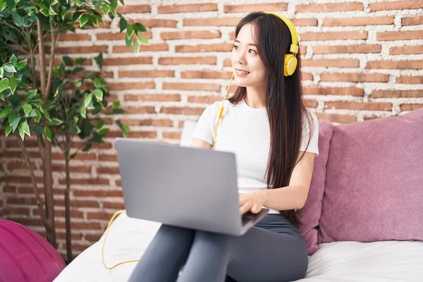 Young Chinese Woman Using Laptop Headphones Sitting Bed Bedroom — Stok fotoğraf
