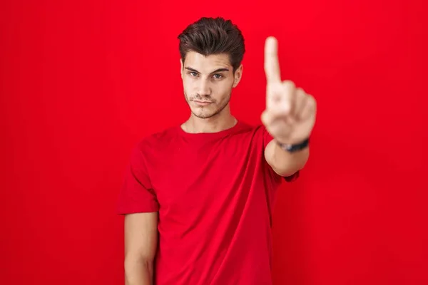 Młody Hiszpan Stojący Nad Czerwonym Tłem Wskazujący Palcem Górę Gniewnym — Zdjęcie stockowe