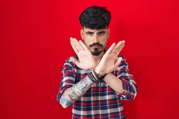 Fiatal Spanyol Férfi Szakállal Áll Piros Háttér Elutasítás Kifejezés Keresztbe — Stock Fotó