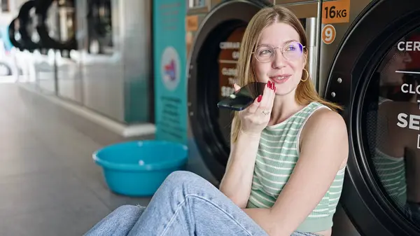 Nuori Blondi Nainen Lähettää Ääniviestin Älypuhelimella Odottamassa Pesukonetta Pesutuvassa — kuvapankkivalokuva