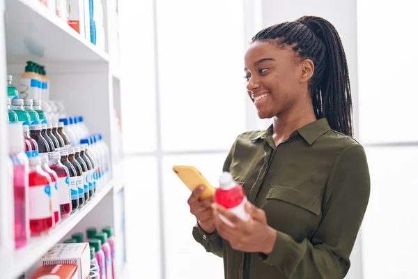 stock image African american woman customer using smartphone holding medicine bottle at pharmacy