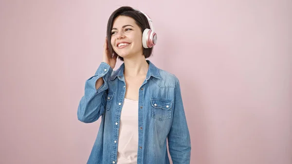若いです白人女性に耳を傾け音楽を身に着けていますヘッドフォン以上隔離されたピンクの背景 — ストック写真